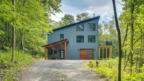 A modern two-story house with a gravel driveway, surrounded by dense forest. - Swanton Retreat w/ Game Room, Hot Tub & Trails! (Swanton)