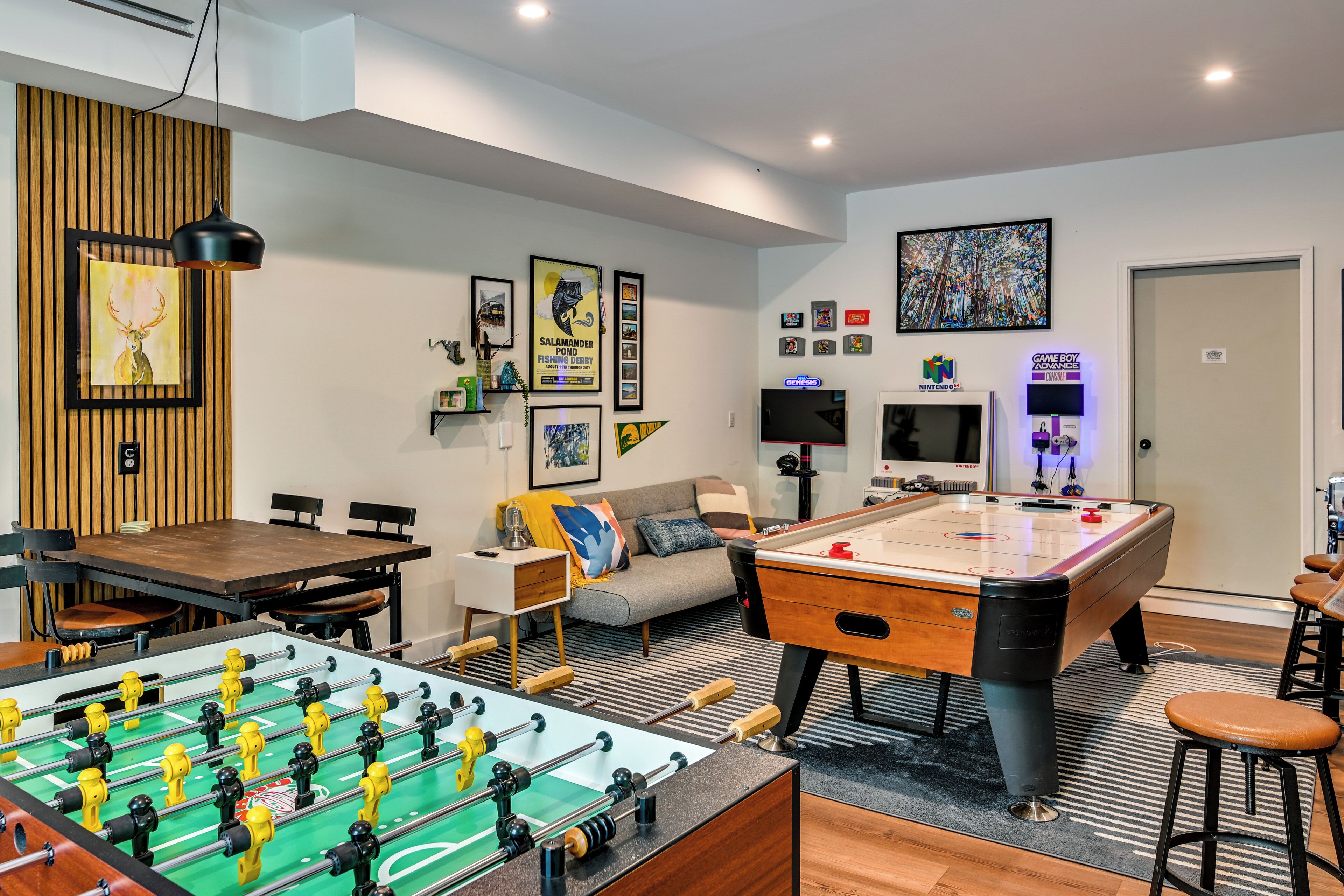 A room with a foosball table, pool table, and a TV.