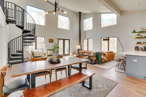 A spacious living area with a wooden dining table, benches, and a spiral staircase. - Swanton Retreat w/ Game Room, Hot Tub & Trails! (Swanton)