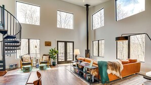 A spacious living room with a large sofa, a dining table, and a spiral staircase. - Swanton Retreat w/ Game Room, Hot Tub & Trails! (Swanton)
