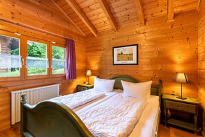 Ein Zimmer einer Holzblockhütte mit einem Bett, zwei Nachttischen, einem gerahmten Bild und einem Fenster mit Vorhängen.