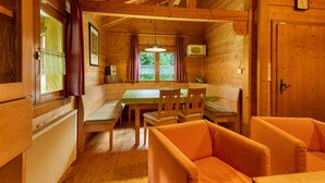 A wooden cabin interior with a dining table, chairs, a sofa, a window with curtains, and a clock on the wall. - Apartment 'Blockhaus Hedwig Zwei' with Shared Pool, Private Terrace and Wi-Fi (Stamsried)