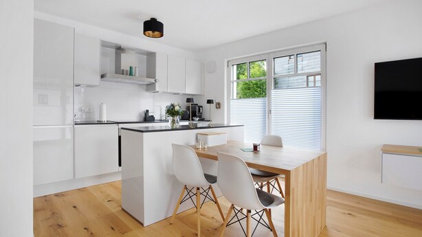A modern kitchen with white cabinetry, a wooden dining table, and two chairs.