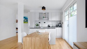 A modern kitchen with white cabinets, a wooden dining table, and a black pendant light.
