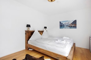 A bed with white linens, two bedside lamps, and a painting of a snowy mountain scene. - Apartment 'Design Ferienwohnung Am Chiemsee' with Private Terrace, Private Garden and Wi-Fi (Breitbrunn am Chiemsee)