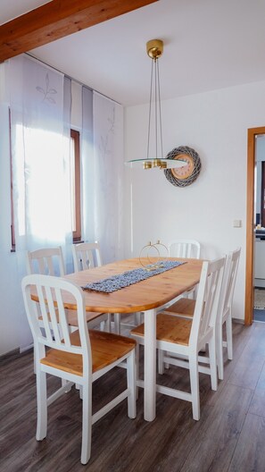Un comedor con una mesa de madera, sillas blancas, una lámpara colgante y un reloj de pared.
