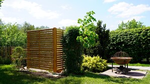 Un jardin entouré d’une clôture en bois, agrémenté d’une mangeoire à oiseaux en métal et d’une grande variété de plantes.