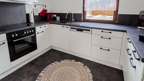 Une cuisine moderne avec des meubles blancs, un four noir, un lave-vaisselle et un tapis à motifs.
