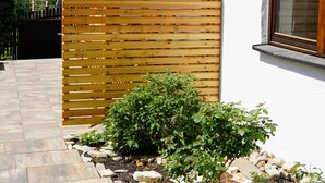 Une maison moderne avec une terrasse en bois, un petit jardin et une fenêtre.