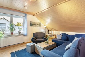 A modern living room with a sloped ceiling, a blue sofa, a black armchair, a wooden coffee table, and a radiator.