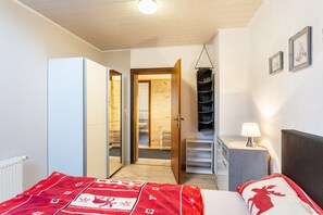 A bedroom with a bed, a wardrobe, a desk, and a hanging shelf.
