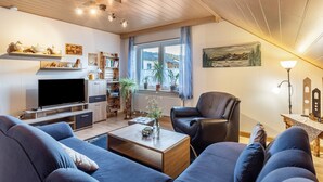 Una sala de estar con televisor, sofás, una mesa de centro y una estantería.