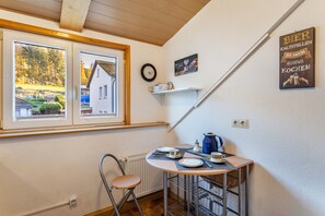 A small kitchen with a table set for two, a chair, a radiator, and a window with a view of a house and trees.