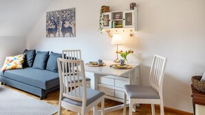 Een gezellige kamer met een bank, twee witte stoelen, een kleine tafel met een lamp en een boekenplank.