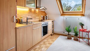 Een moderne keuken met houten kastjes, een inbouwoven, een raam met uitzicht en potplanten.