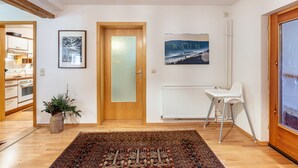 Una habitación con suelo de madera, un radiador, una silla blanca, un cuadro enmarcado y una puerta con cristal esmerilado.