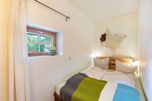 A bedroom with a bed, a window, a wall-mounted light, and a wall decoration. - Holiday Apartment 'Kammbühlhof' with Sauna, Mountain View, Private Terrace & Wi-Fi (Sankt Blasien)