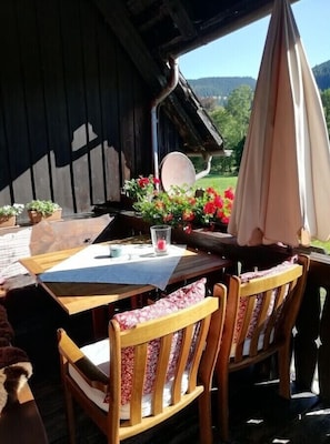 An outdoor seating area with wooden tables and chairs, a flower arrangement, and a view of the landscape. - Holiday Apartment 'Kammbühlhof' with Sauna, Mountain View, Private Terrace & Wi-Fi (Sankt Blasien)