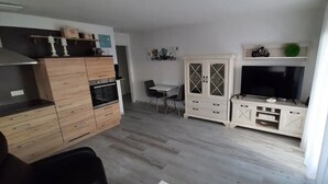 Une cuisine compacte comprenant un coin repas, un téléviseur et un meuble sur lequel est apposé un panneau indiquant « MAISON ».