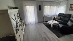 Un salon avec un canapé en cuir noir, une table basse blanche et un meuble blanc agrémenté d’objets décoratifs.