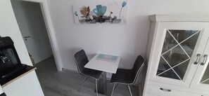 Un pequeño comedor con una mesa y dos sillas, un armario con puertas de vidrio y una obra de arte colgada en la pared.