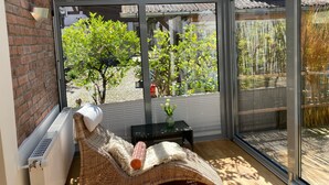A sunlit room with a glass wall, a wicker sofa, a small table with a vase, and a radiator. - Holiday Home 'Ferienhaus bei Juste' with Private Terrace, Shared Garden and Wi-Fi (Schotten)