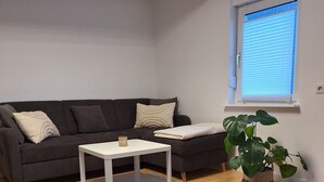 Ein Wohnzimmer mit grauem Sofa, weißem Couchtisch, grauem Teppich und einem Blumentopf.
