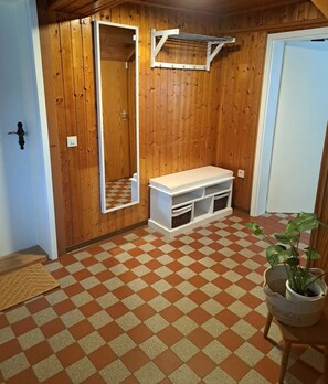 Een kamer met houten wanden, een geruit vloertje, een bank, een spiegel en een hangende kapstok.