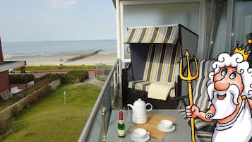 A balcony with a view of the beach, a table with a bottle, glasses, and a teapot, and a cartoon character holding a trident.