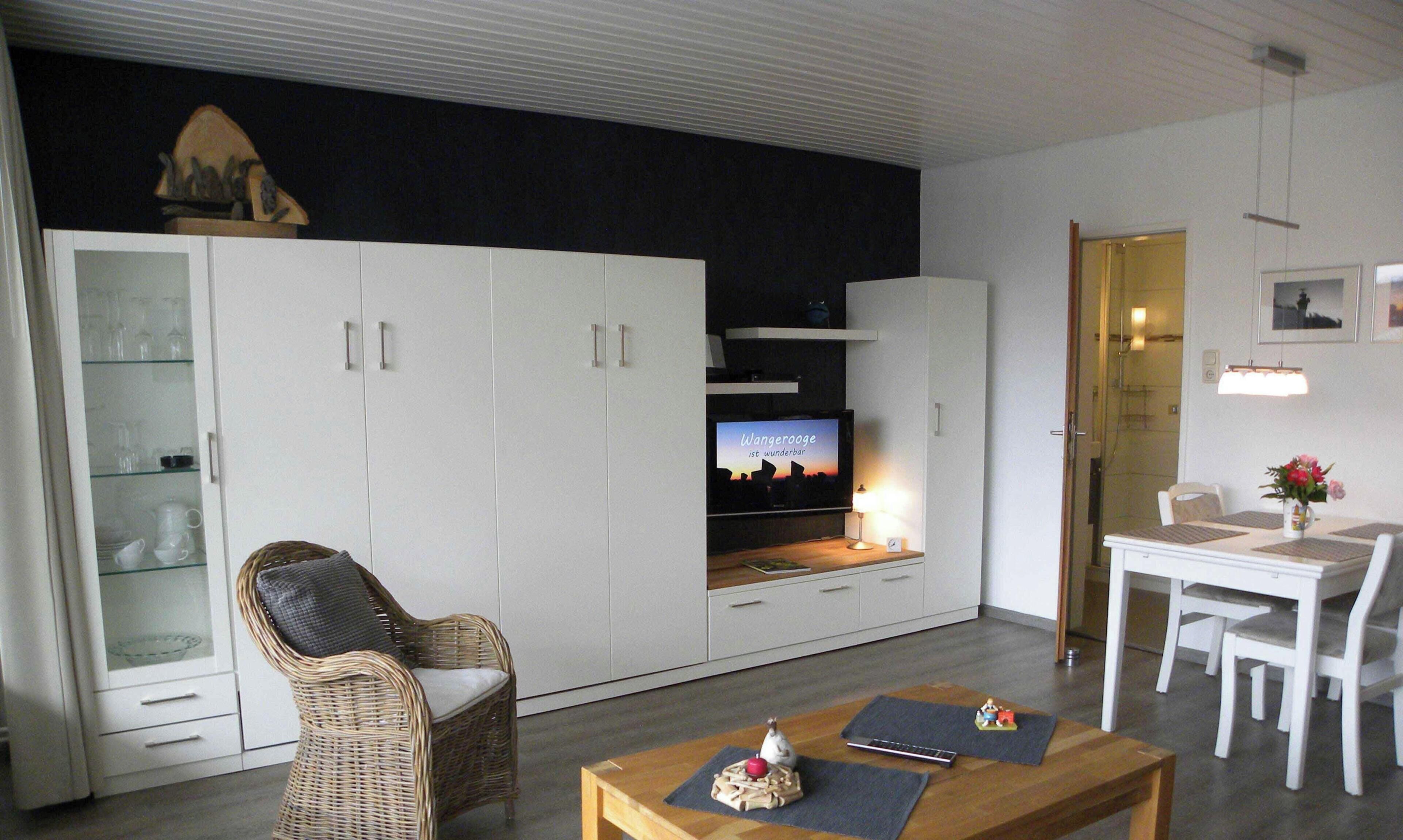 A modern living room with a television, wicker chair, dining table, and white cabinets.