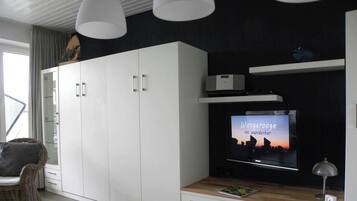 Una sala de estar moderna con televisor de pantalla plana, armarios blancos, una silla de mimbre e iluminación colgante.
