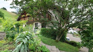 Una casa con tetto spiovente, un vialetto in pietra che conduce all'ingresso e vegetazione rigogliosa tutt'intorno.