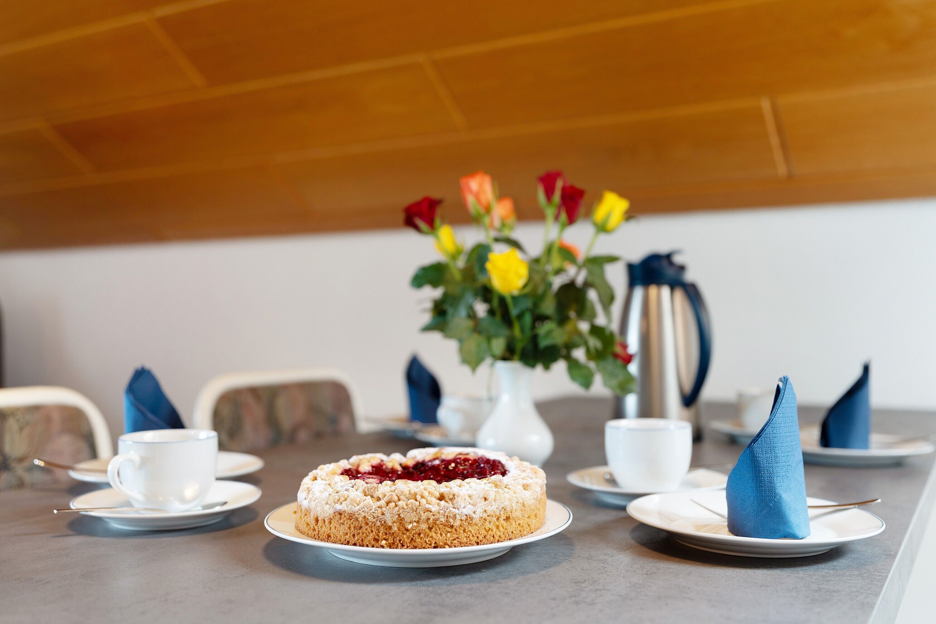Une table à manger avec un gâteau, des tasses blanches, des soucoupes et des serviettes bleues.