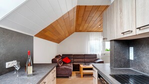 Eine moderne Küche mit Einbauofen, ein Essbereich mit Holztisch und ein Wohnbereich mit Sofa.