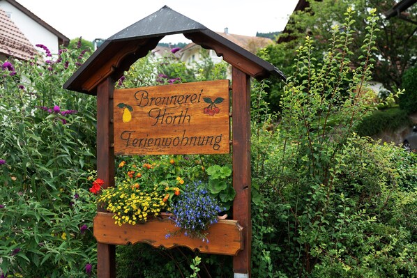 Une enseigne en bois portant les inscriptions « Brennerei Nord » et « Fleischbröckung », entourée de verdure et de fleurs.