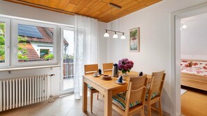 Ein Essbereich mit Holztisch, Stühlen, einem Heizkörper, einem Fenster mit Vorhängen und Blick auf ein Haus mit Solaranlage.