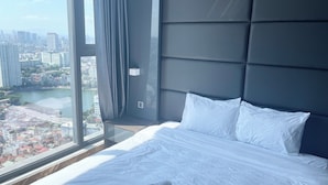 A modern hotel room with a large bed, white linens, and a view of a cityscape through a large window. - Vinhomes Metropolis Ba Dinh - Apartment  (Hanoi)