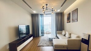 A modern living room with a flat-screen TV, a sofa, a coffee table, and a small refrigerator. - Vinhomes Metropolis Ba Dinh - Apartment  (Hanoi)