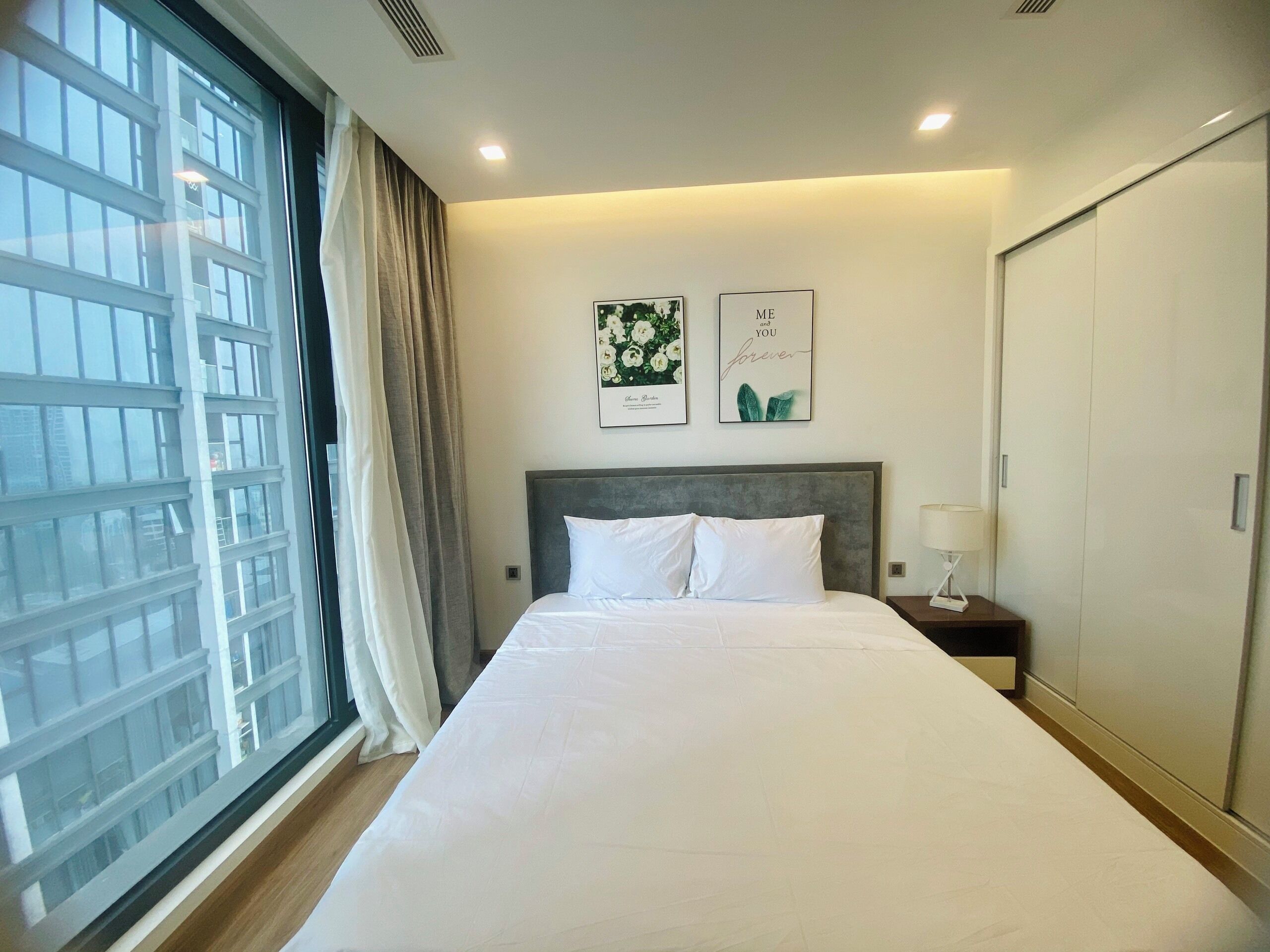 A hotel room with a large bed, a nightstand, a lamp, a wardrobe, and two framed pictures on the wall.
