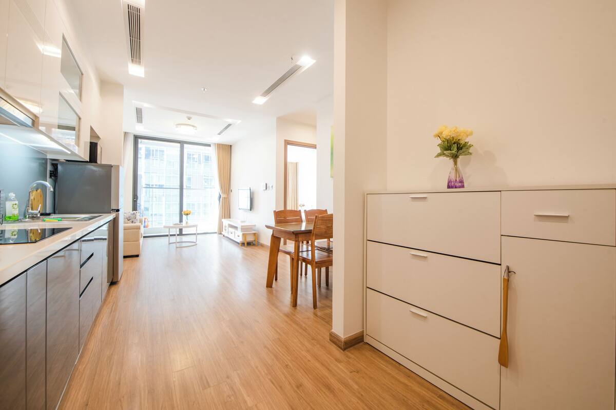Une cuisine moderne avec un plancher en bois, un coin repas comprenant une table et des chaises, et un meuble blanc orné d’un vase de fleurs.