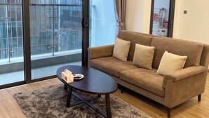 A modern living room with a brown sofa, a dark coffee table, and a large window with a view of a building. - Vinhomes Metropolis Ba Dinh - Apartment  (Hanoi)