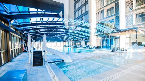 An indoor swimming pool with a curved roof structure, surrounded by a tiled floor and a staircase leading to the pool area. - Vinhomes Metropolis Ba Dinh - Apartment  (Hanoi)