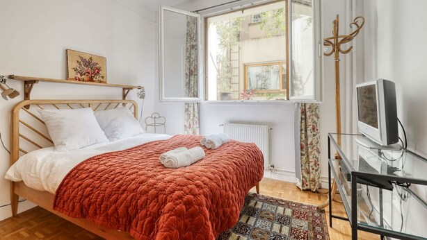 Ein Schlafzimmer mit einem Bett, einem Fenster, einem Fernseher und einem Regal mit einem Bild.