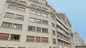 Ein mehrstöckiges Gebäude mit einer beigefarbenen Fassade, großen Fenstern und Balkonen mit Geländern.