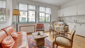 Ein modernes Apartment mit Wohnzimmer, Essbereich und Küche. Große Fenster, ein Sofa, ein Couchtisch und ein Teppich sind vorhanden.