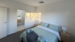 Une chambre à coucher comprenant un lit, des tables de chevet, une commode, un miroir et une porte.