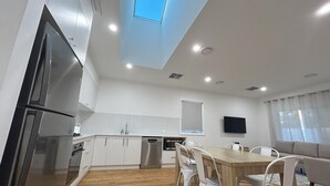 Une cuisine moderne avec des meubles blancs, un réfrigérateur en acier inoxydable et une table à manger en bois, assortie de chaises blanches.