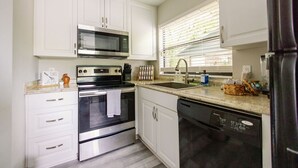 A kitchen with white cabinets, stainless steel appliances, a microwave, oven, dishwasher, and a window with blinds. - Quiet 1-Story Townhome off I-75 by UF, Shands, VA, Celebration Pointe &Shopping! (Gainesville)