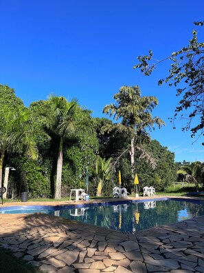 A swimming pool with stone tiles, surrounded by lush greenery and trees. - Pousada dos Ypês (Artur Nogueira)