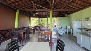 Un comedor interior con mesas y sillas de madera, suelo de baldosas y un techo alto con vigas a la vista.